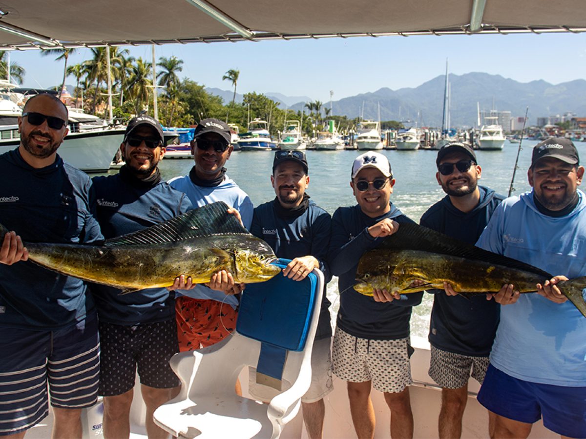 Seven men happily holding two large Dorado fish on the back of a charter boat in Puerto Vallarta.