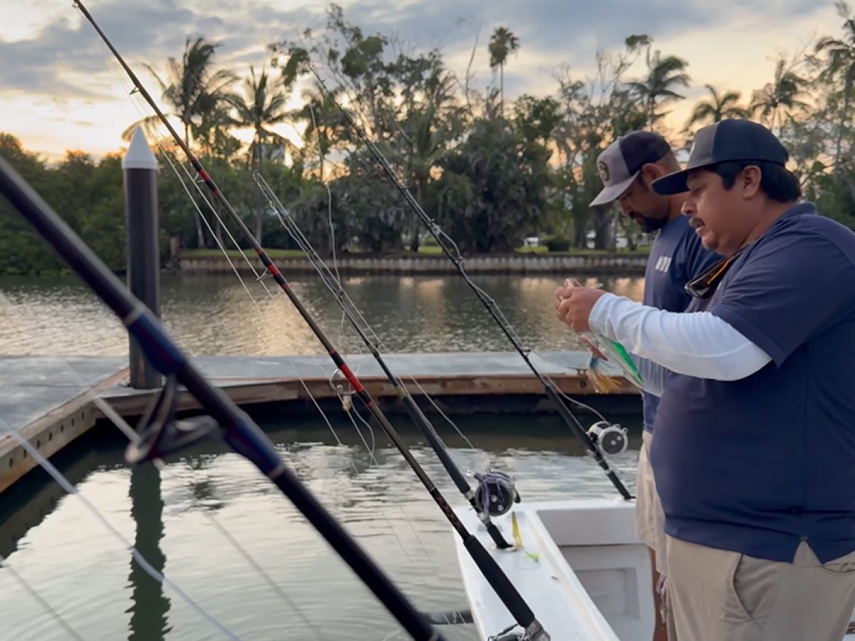 Two crew members preparing heavy-duty hooks on the back deck of a fishing charter boat.