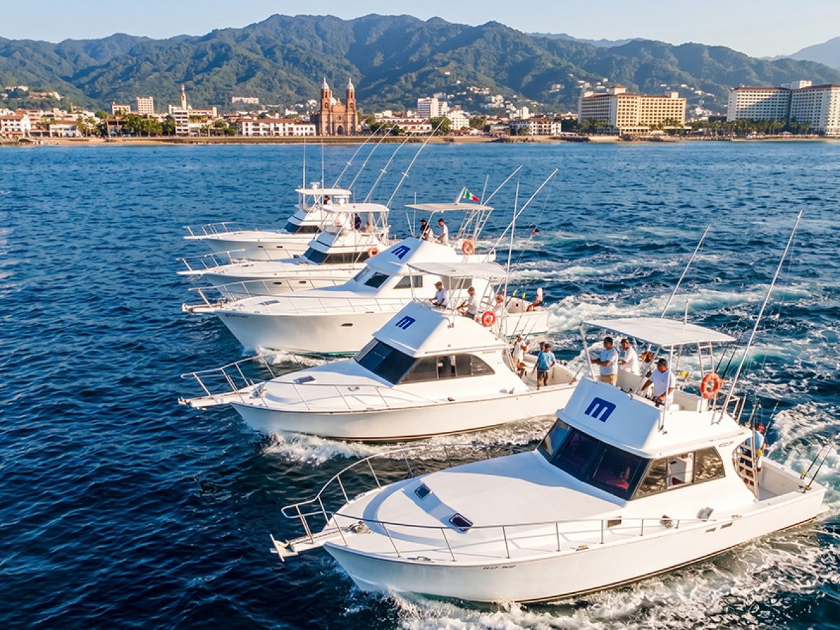 Five sportfishing boats navigating together with the Puerto Vallarta skyline in the background.