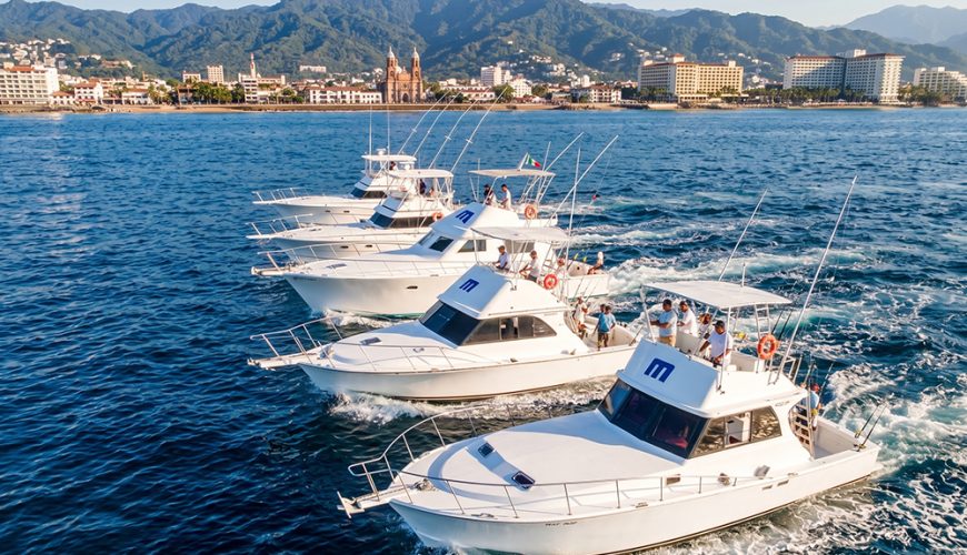 Five sportfishing boats navigating together with the Puerto Vallarta skyline in the background.