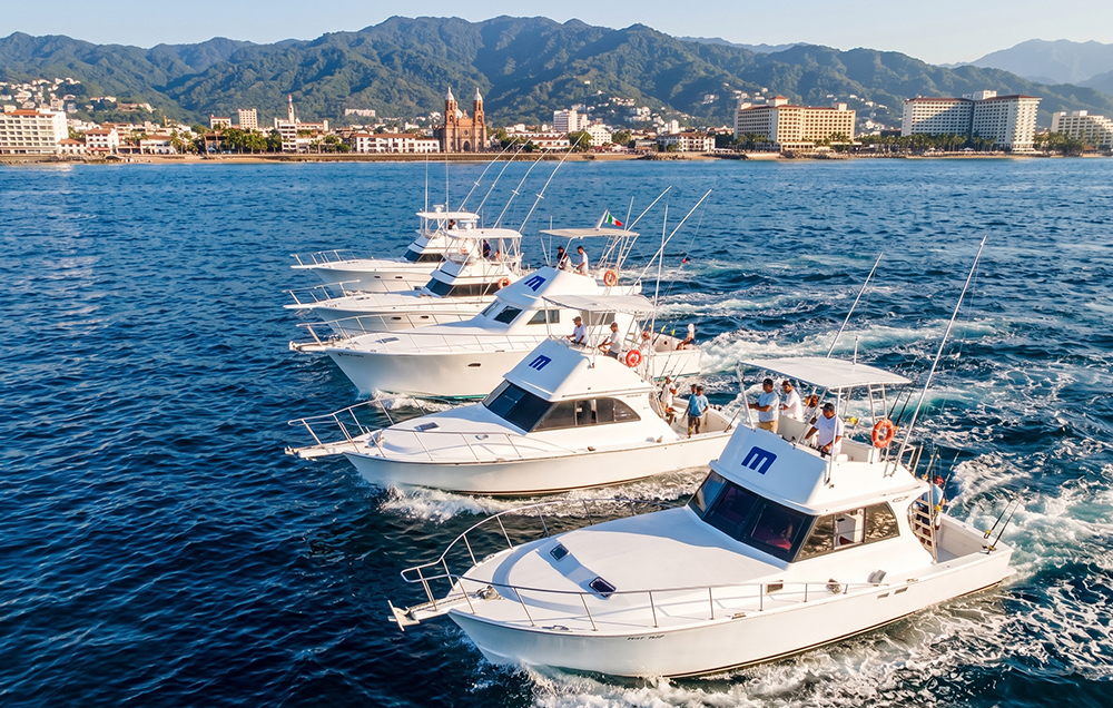 Five sportfishing boats navigating together with the Puerto Vallarta skyline in the background.